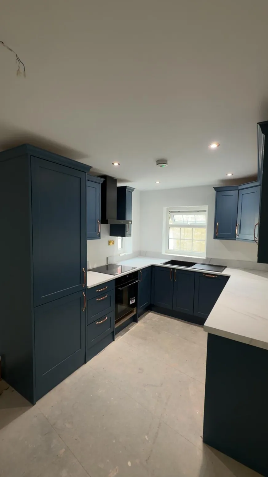 Matt blue L-shaped kitchen with white splashback tiles